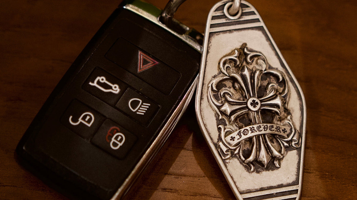 Fleur-de-Lis Crest Silver Keychain, front view beside a car key