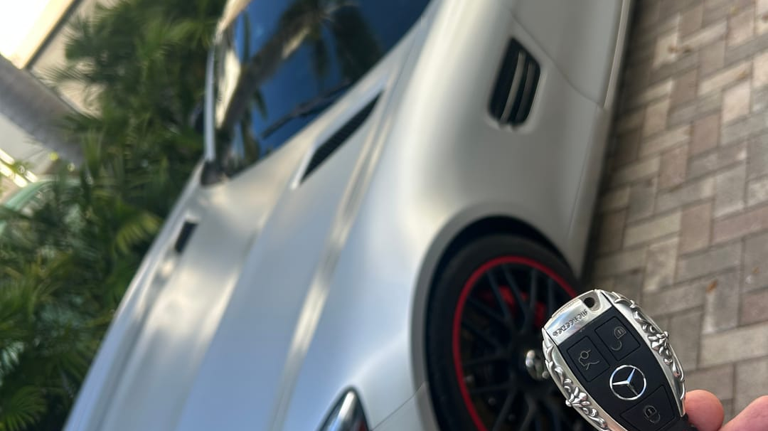 Customer car photo showing an IGNIS ARGENTUM key case held beside a premium sports car after installation