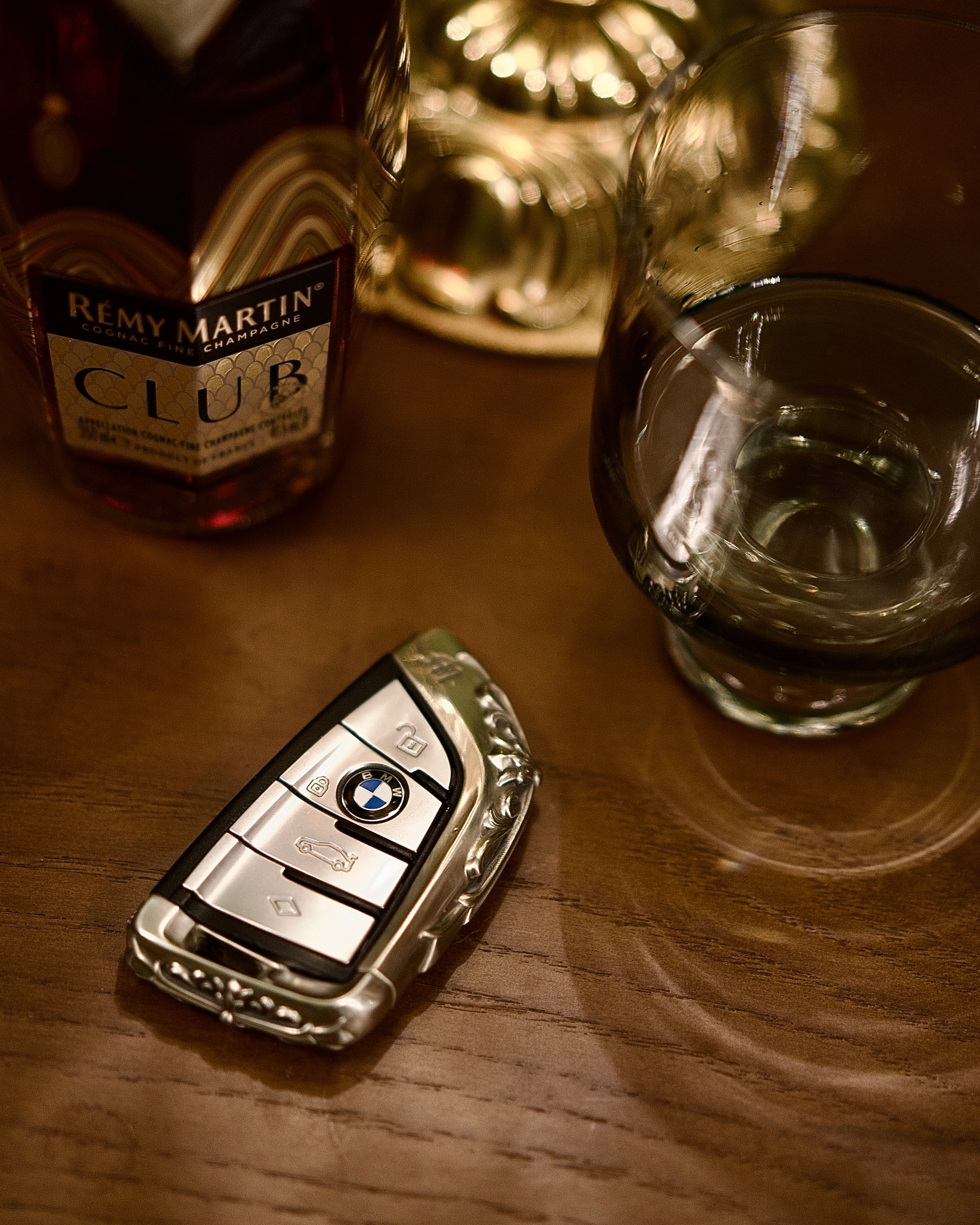 Handmade silver key case for BMW flat lay on wooden table with whiskey glass warm ambient lighting showcasing masculine heft and understated luxury