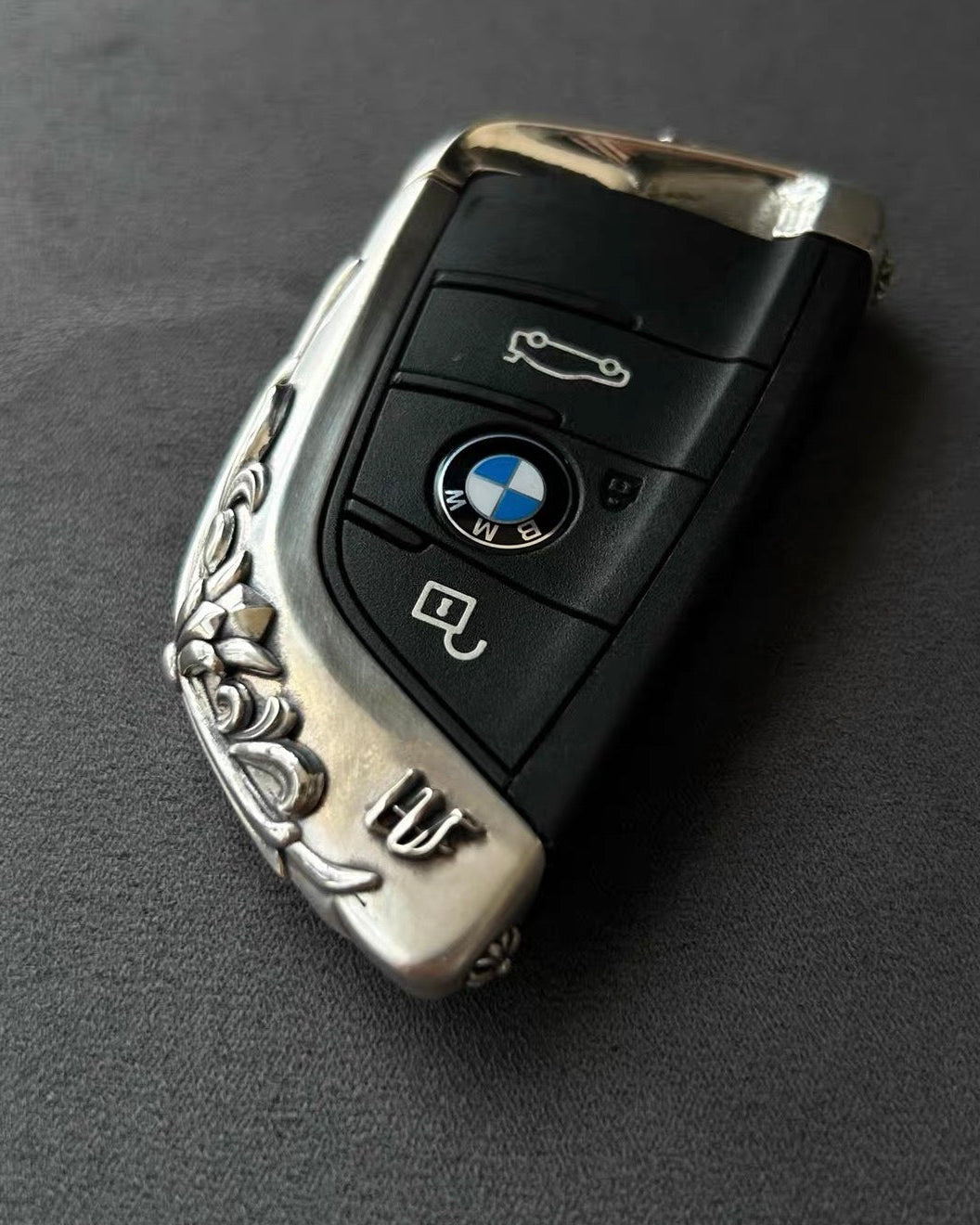BMW slim edge key case front view on dark gray background showing precision button cutouts and engraved surface without interfering lock unlock functions