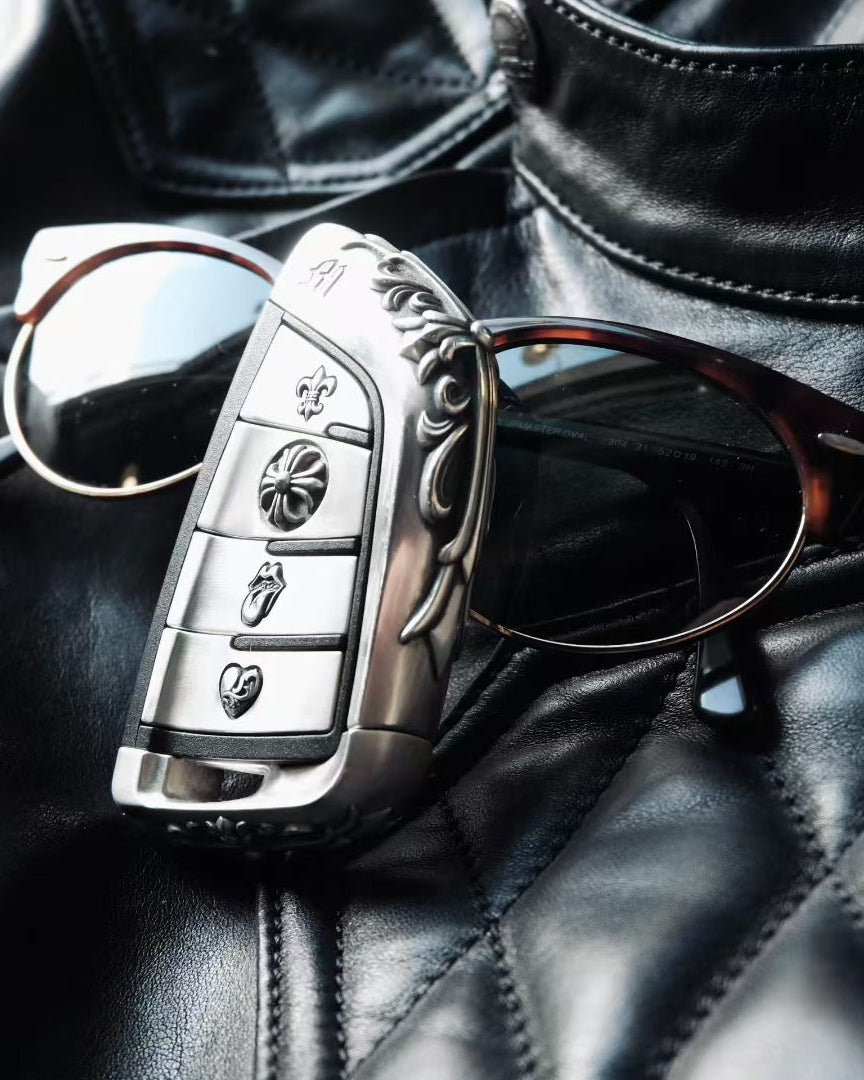 BMW slim edge key case paired with metal sunglasses on black leather background suggesting automotive interior and premium accessories coordination