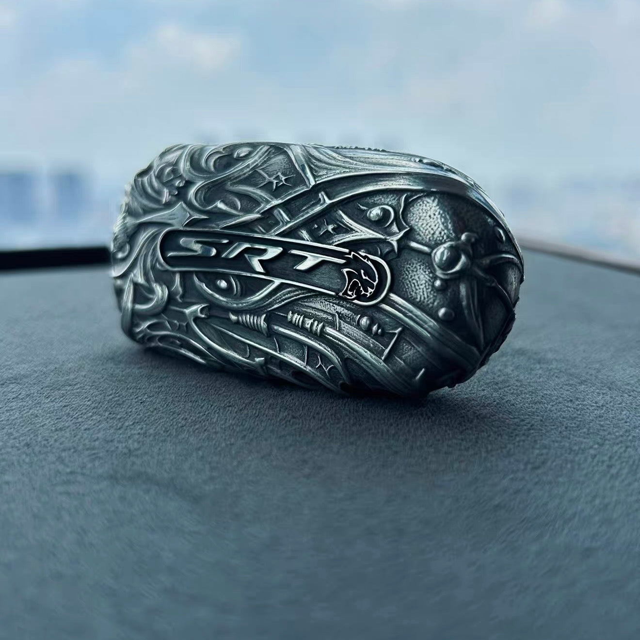 Sterling silver Dodge key case displayed on car dashboard, showcasing complete dragon head sculpture and hand-carved ornamental patterns with substantial presence