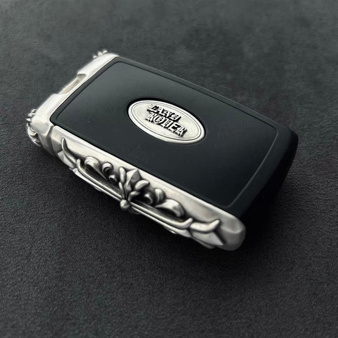 Side view of Land Rover key case highlighting intricate silver engraving with baroque scrollwork and floral patterns, polished edges and substantial hand-feel