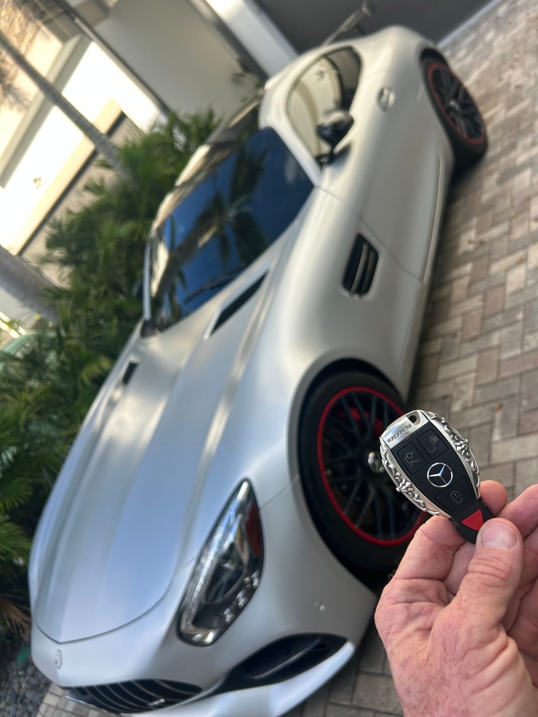 Customer car photo showing an IGNIS ARGENTUM key case held beside a premium sports car after installation