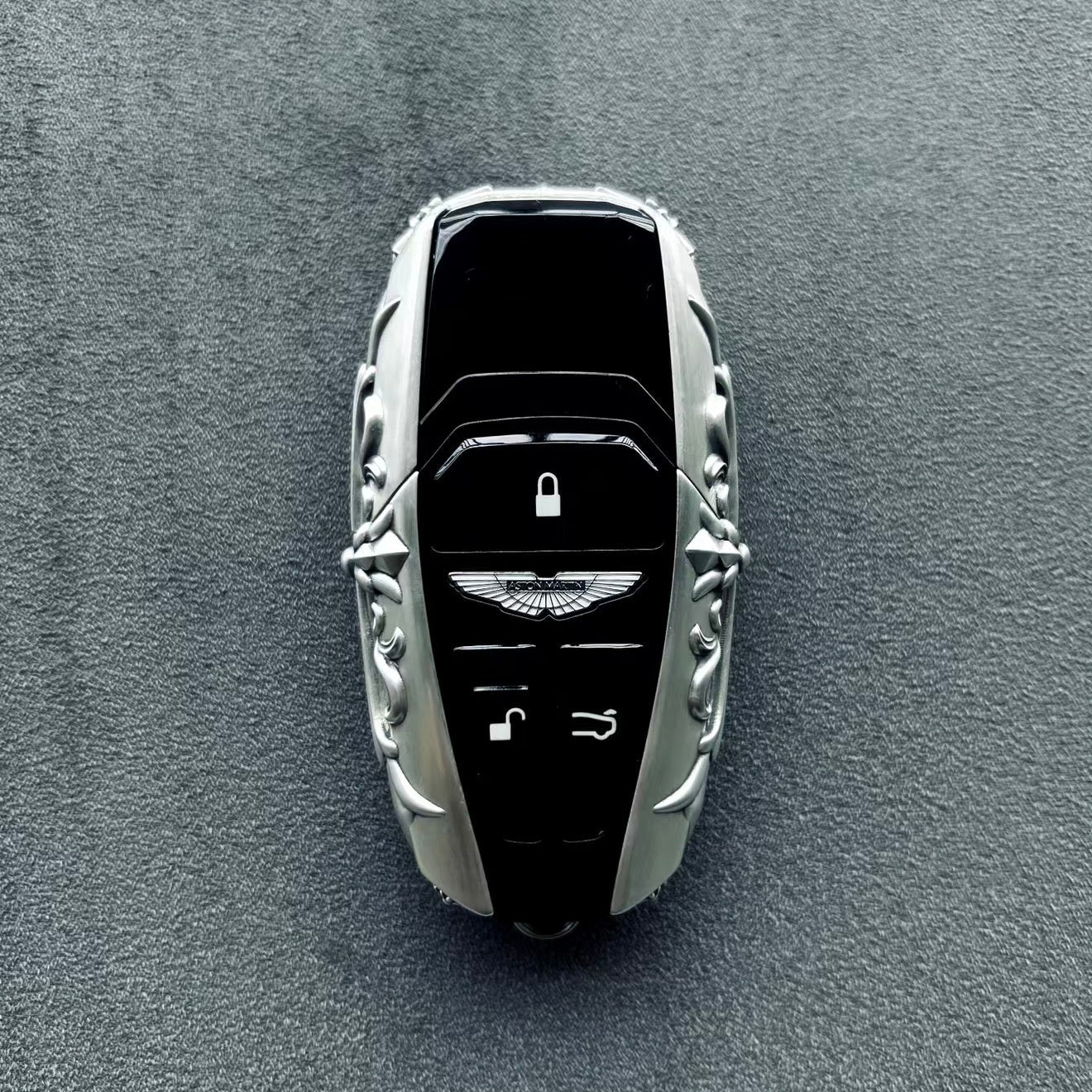 Aston Martin handcrafted sterling silver key case with key fully embedded, top-down perspective showing seamless integration and uniform engraving around solid silver perimeter