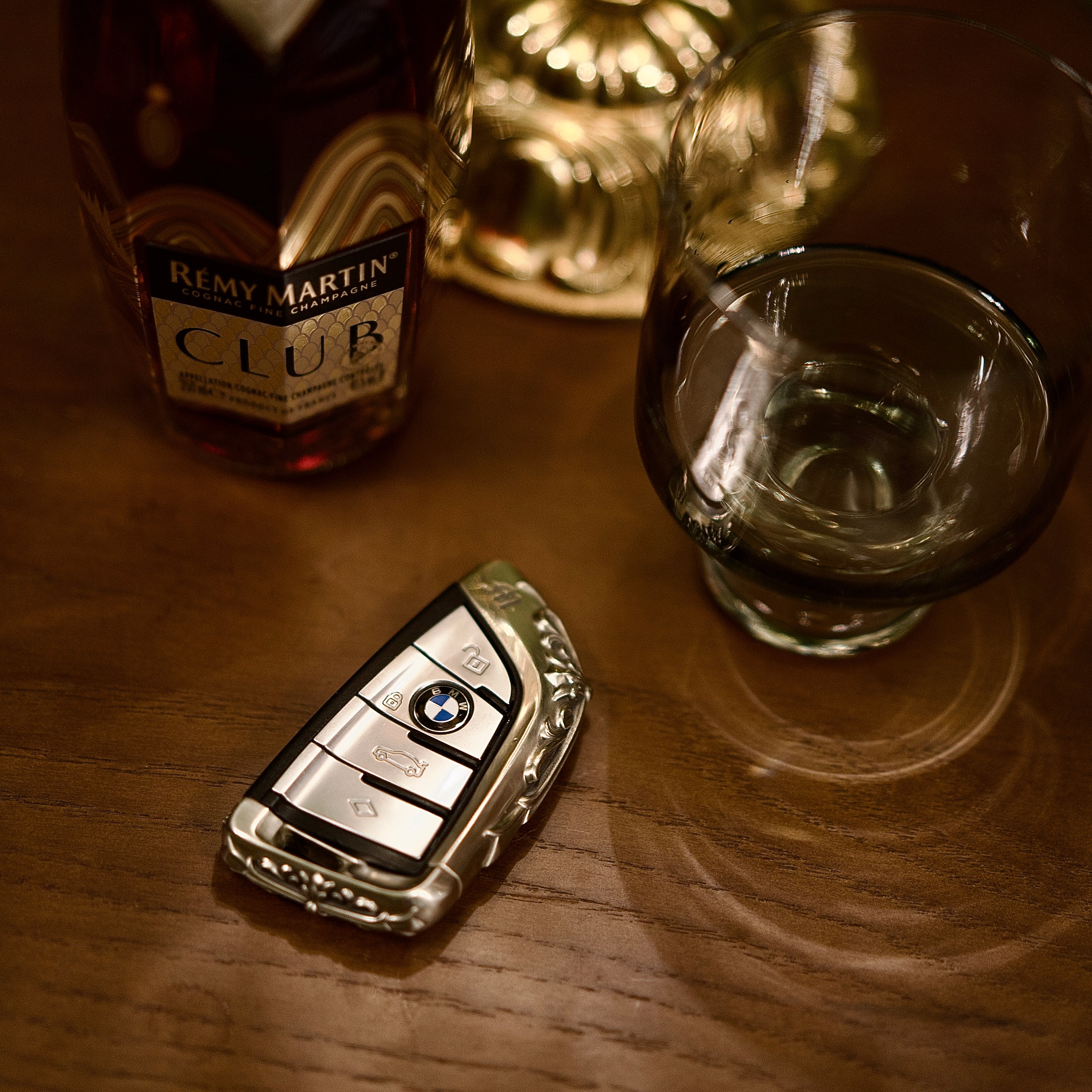 Handmade silver key case for BMW flat lay on wooden table with whiskey glass warm ambient lighting showcasing masculine heft and understated luxury