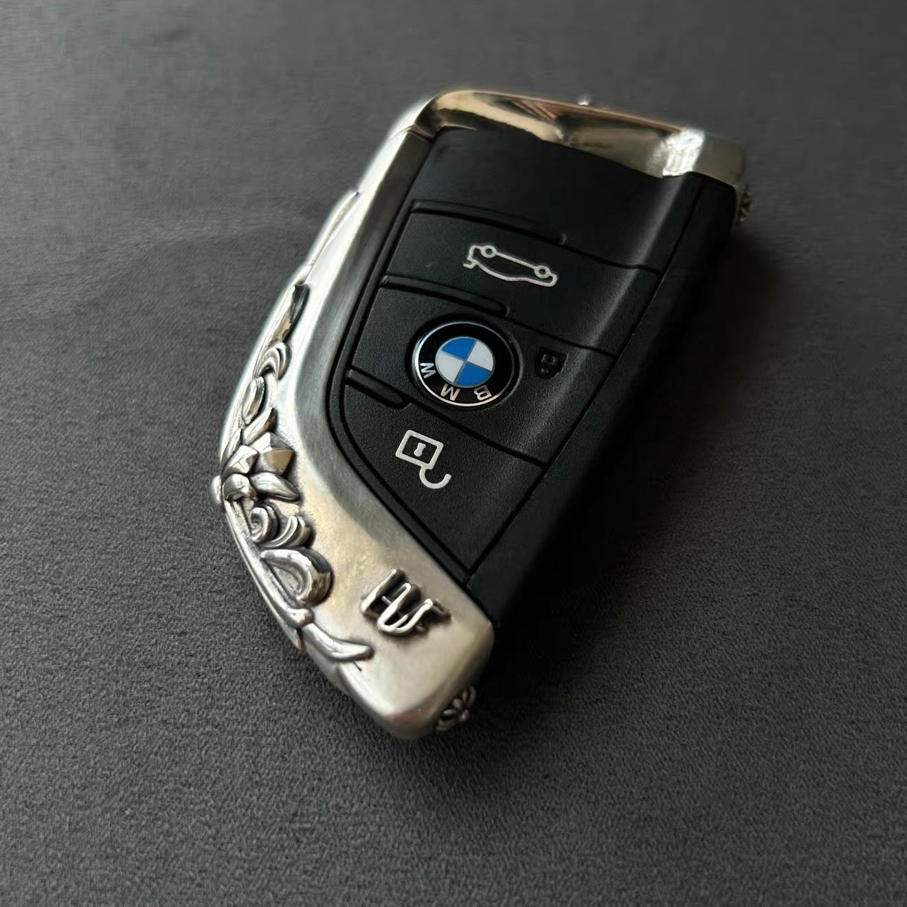 BMW slim edge key case front view on dark gray background showing precision button cutouts and engraved surface without interfering lock unlock functions
