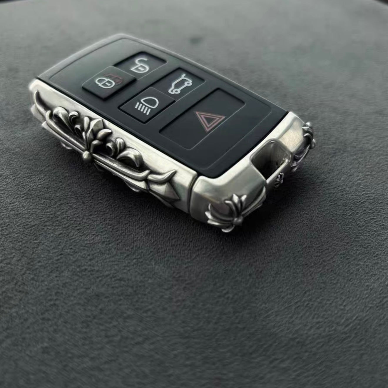 Land Rover key fitted into custom silver engraved case showing full functionality with 5-button layout (lock, unlock, trunk, hazard, engine) and sleek design