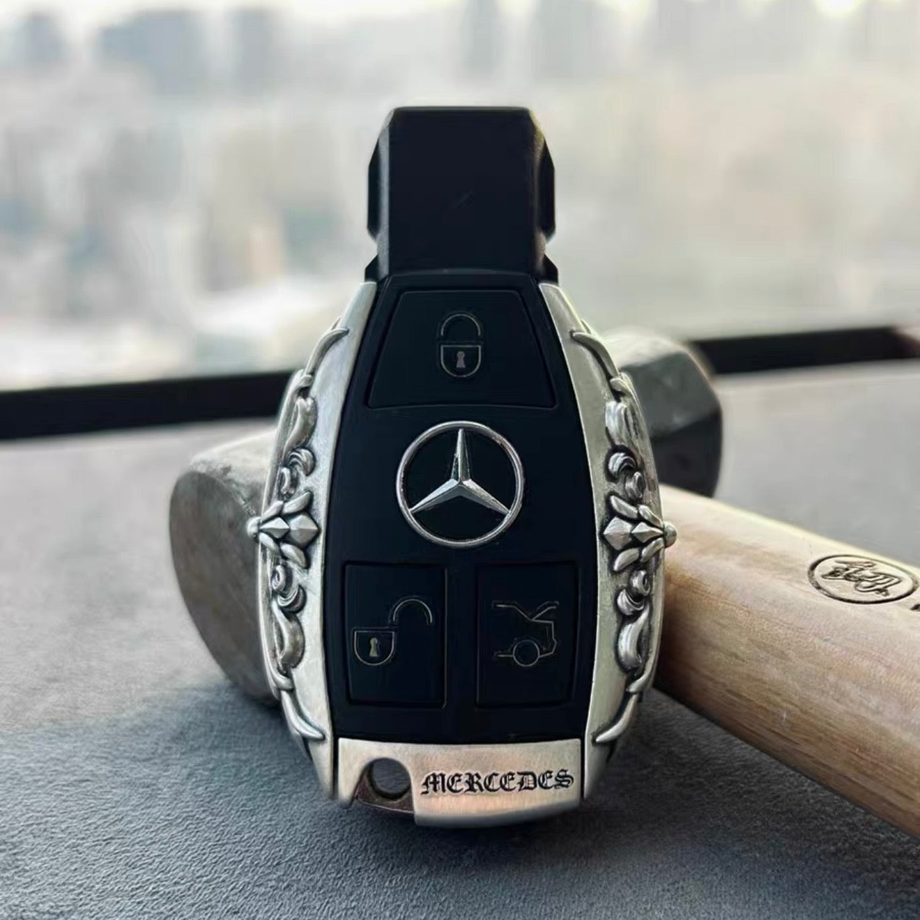 Mercedes Classic Oval handcrafted key case Nickel Silver front view with ornate floral oval engraving and three-pointed star emblem on wooden stand