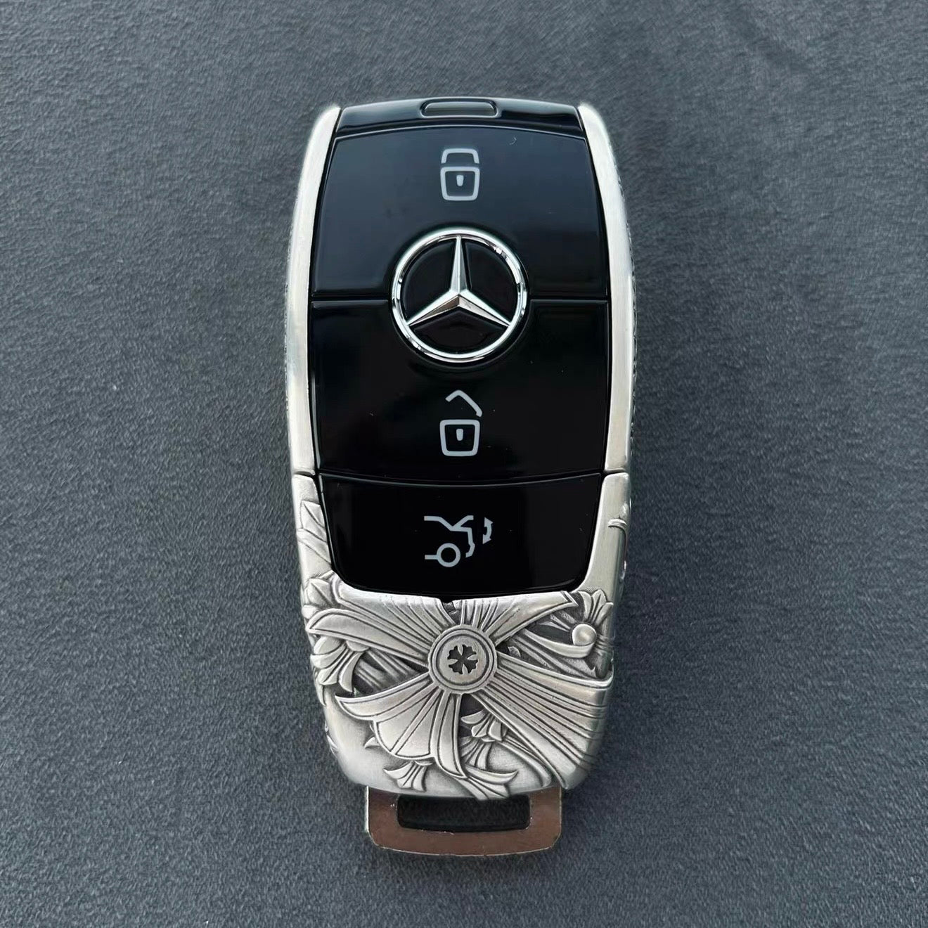 Handmade silver key case for Mercedes flat lay on wooden table with whiskey glass warm ambient lighting showcasing masculine heft and density