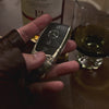 Substantial silver key case for Mercedes owner handheld perspective next to whiskey glass showcasing considerable presence in daily carry